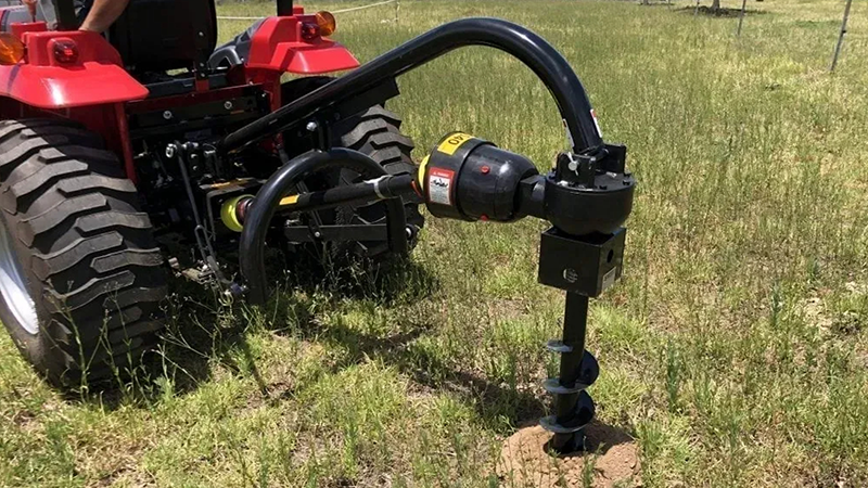 Red tractor in close-up front view actively operating a post hole digger on grassy farmland