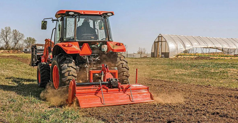 Rotary tiller working in farmland soil preparation with tractor PTO drive